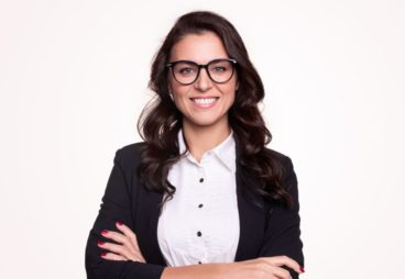 Happy successful adult businesswoman in formal outfit and stylish glasses smiling and looking at camera while standing with arms crossed against white background
